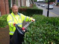 contractor in hi-vis litter picking around shrubbery