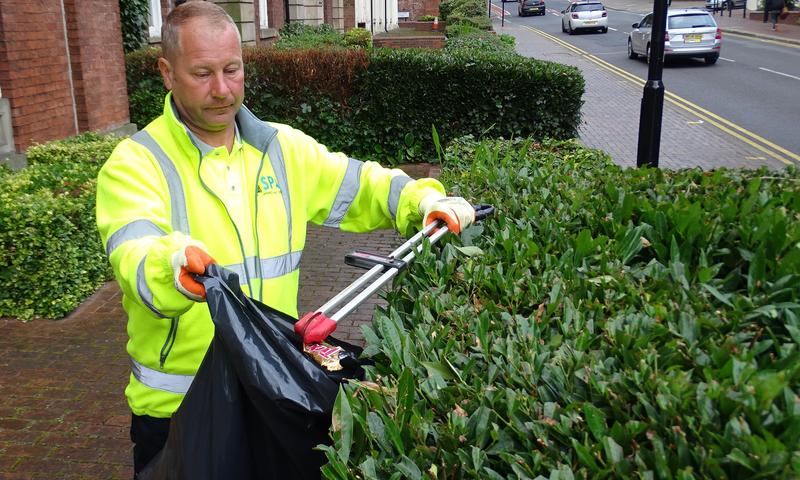 contractor in hi-vis litter picking around shrubbery