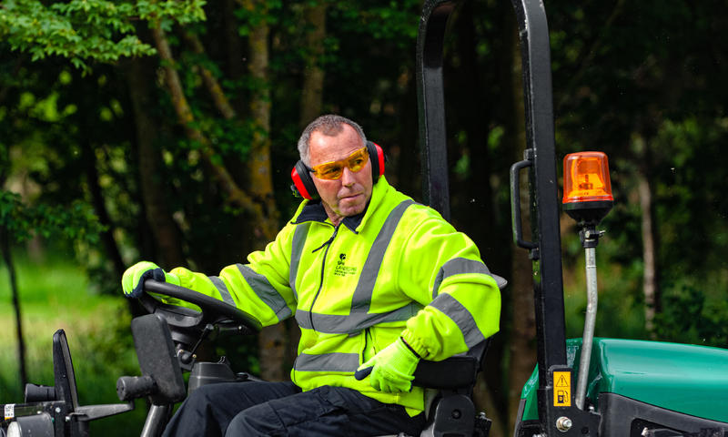 landscape contractor in hi-vis riding a Ransomes mower